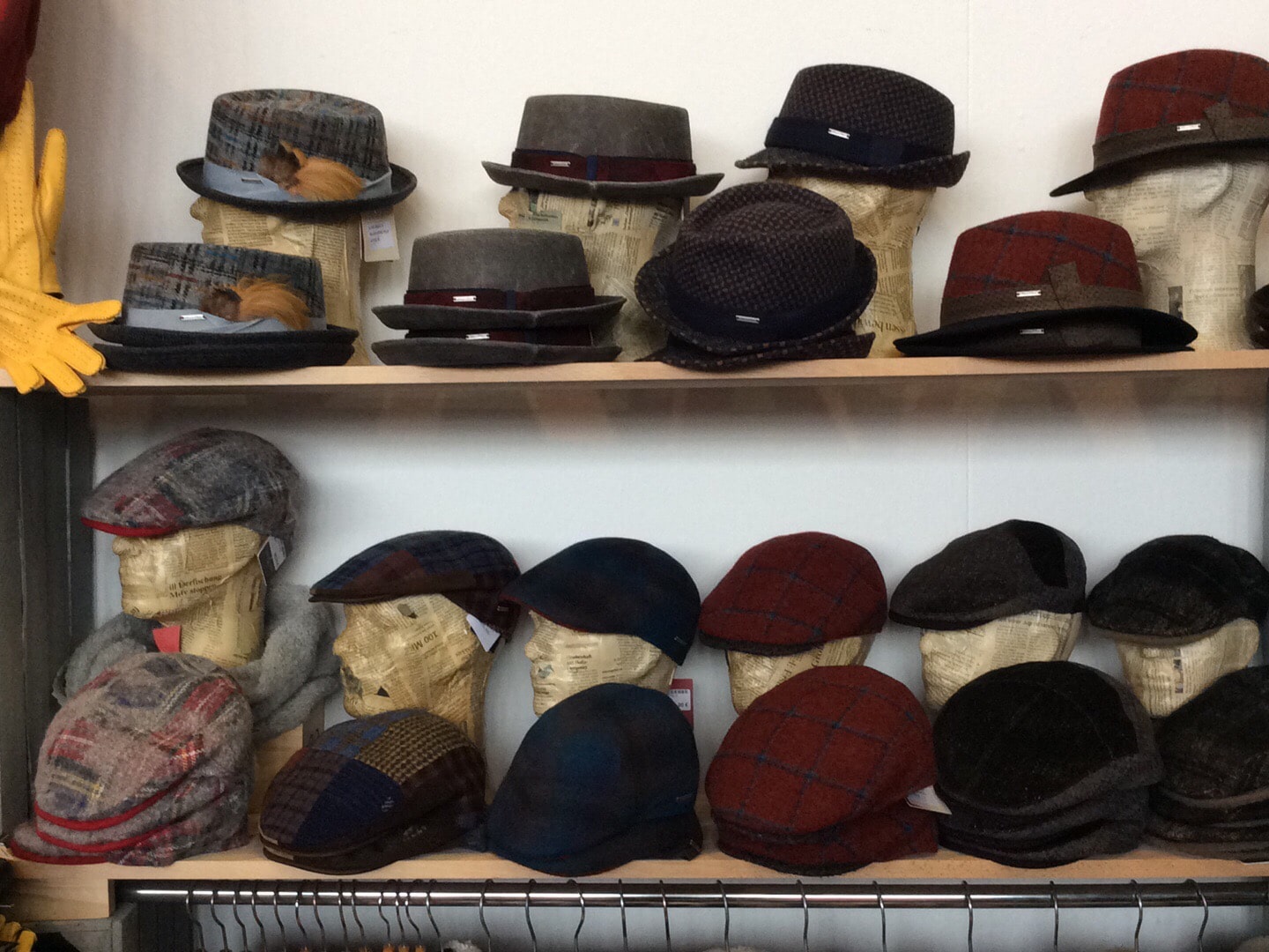 Hier sieht man auf zwei Regalebene aufgereihte Herrenhüte in verschiedenen Modellen, Farben und Formen