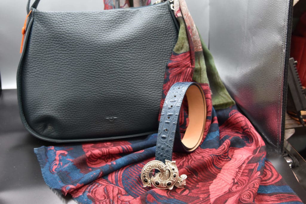 Eine schwarze Lederhandtasche mit einem schwarzen Gürtel und einer goldenen Brosche